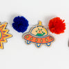 Colorful space-themed wood cutouts including planets, sun, alien, rocket, and astronaut on a white background.