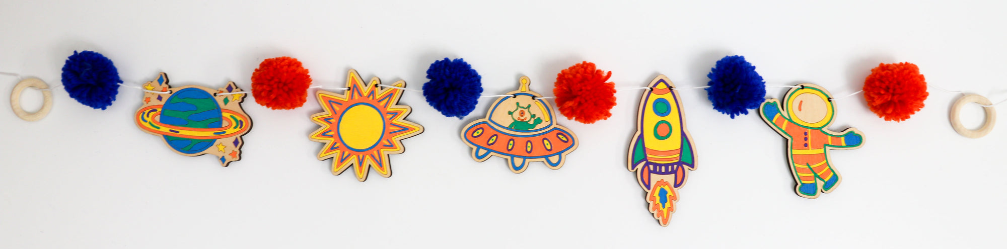 Colorful space-themed wood cutouts including planets, sun, alien, rocket, and astronaut on a white background.