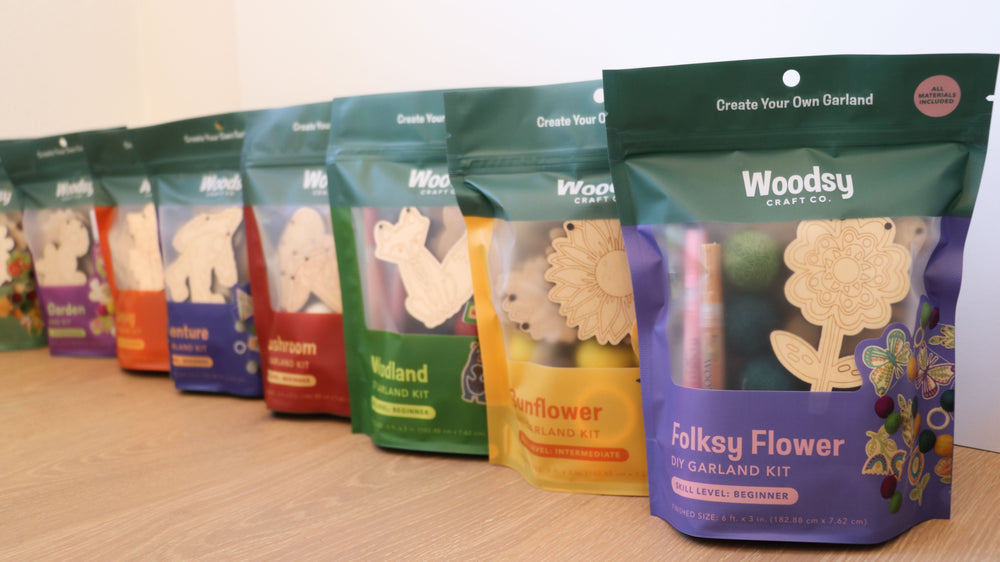Row of colorful 'Woodsy Craft Co.' garden kit packages on a wooden surface.